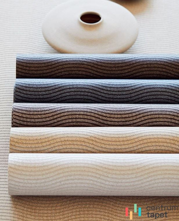 Częściowo rozwinięte rolki różnych wersji kolorystycznych wspólnego falistego deseniu przy jasnym naczyniu