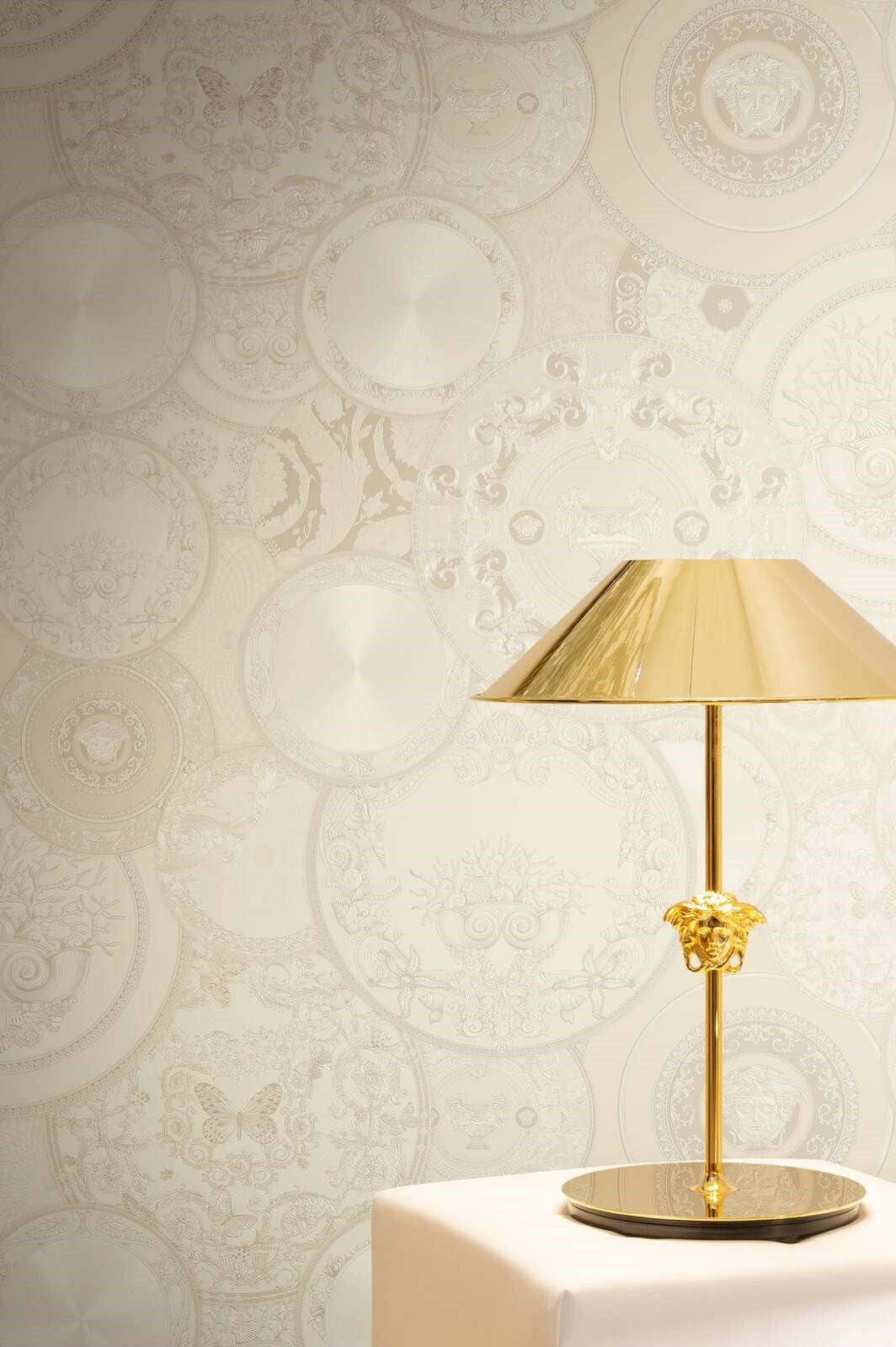 Tapeta Versace VI 79136-1 w kremowe talerze na ścianie za złotą lampą z motywem Meduzy